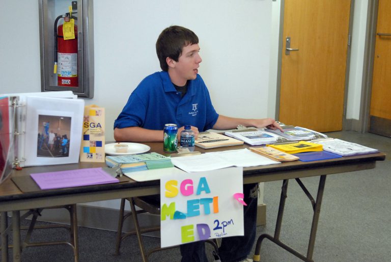 Student government member sitting at table with flyers and sign at eCorsair event.