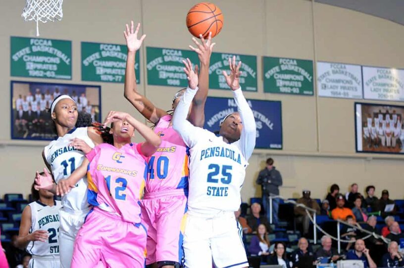 Female basketball players competing in a game at Pensacola State College gymnasium.