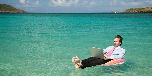 Summer Courses, Yay or Nay? Student working on a laptop while relaxing on a float in the ocean.