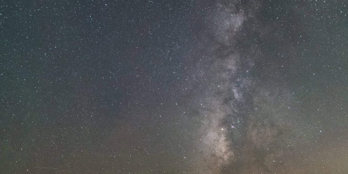 Night sky with the Milky Way and stars over a parking lot during amateur astronomers' event.
