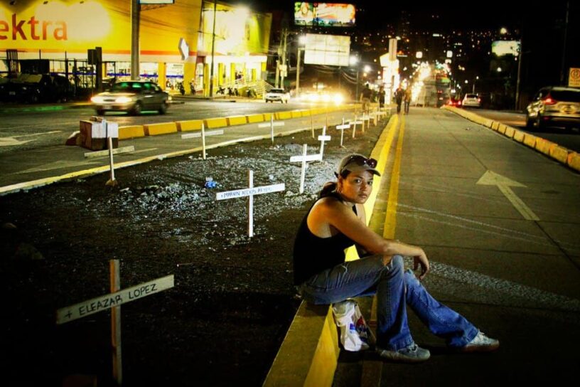 Young woman sitting on the street at night with illuminated crosses symbolizing hope and resilience.