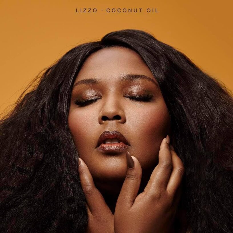 Close-up of Lizzo with long, curly hair and makeup, promoting her album "Coconut Oil".