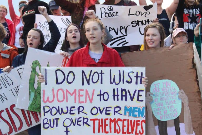 Protesters holding signs advocating for gender equality and women's rights during a student march.
