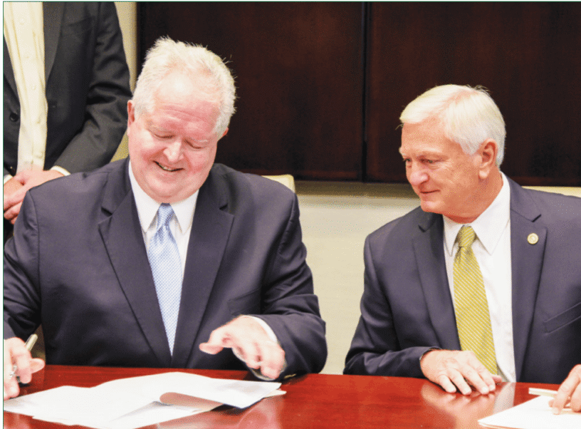 Two men in suits signing documents at FSU Panama City event.