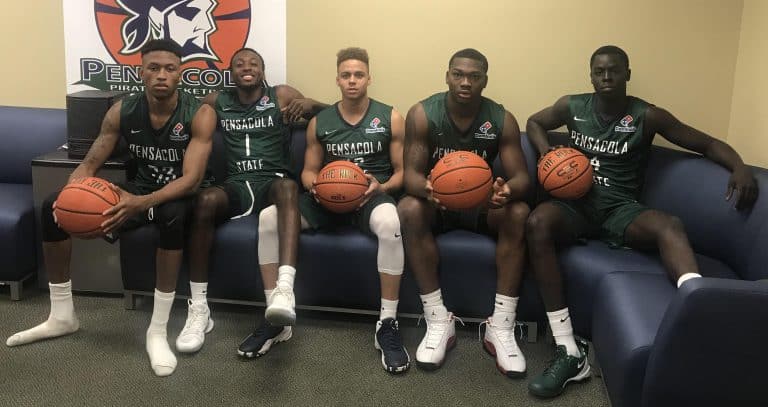 Pensacola State College basketball players sitting with basketballs in locker room.