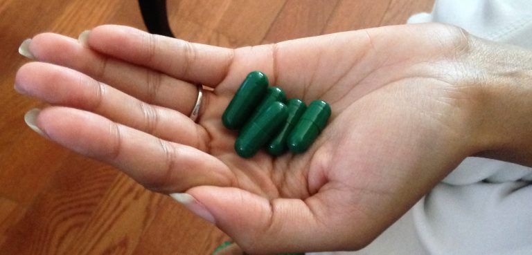 Hand holding green medical marijuana capsules for health treatment.