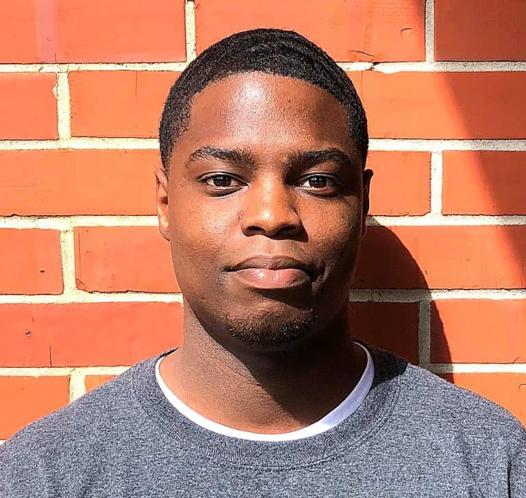 Young man standing against brick wall, promoting softball injury awareness and pre-med education.