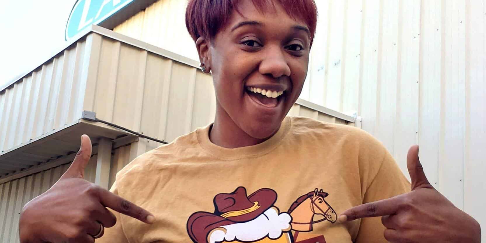 Smiling woman pointing at "Hops for Horses" event sign outside Lamar building.