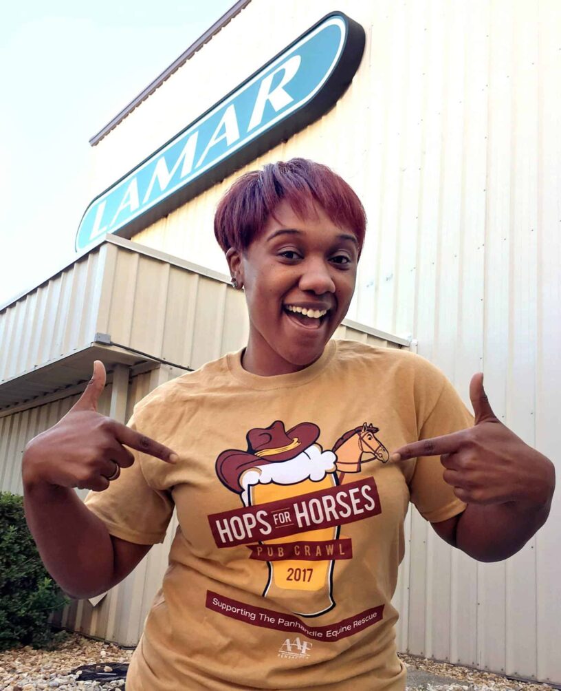 Hops for Horses Event at Lamar Building Smiling woman pointing at "Hops for Horses" event sign outside Lamar building.