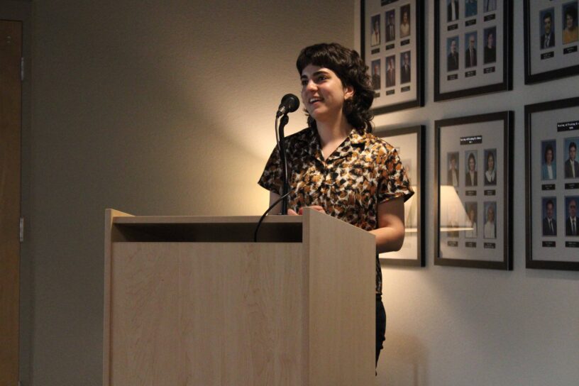 Student speaking at eCorsair event with framed photos in background.