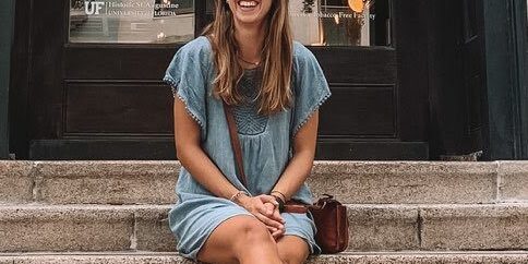 Woman sitting on steps outside eCorsair building, smiling in sunglasses.