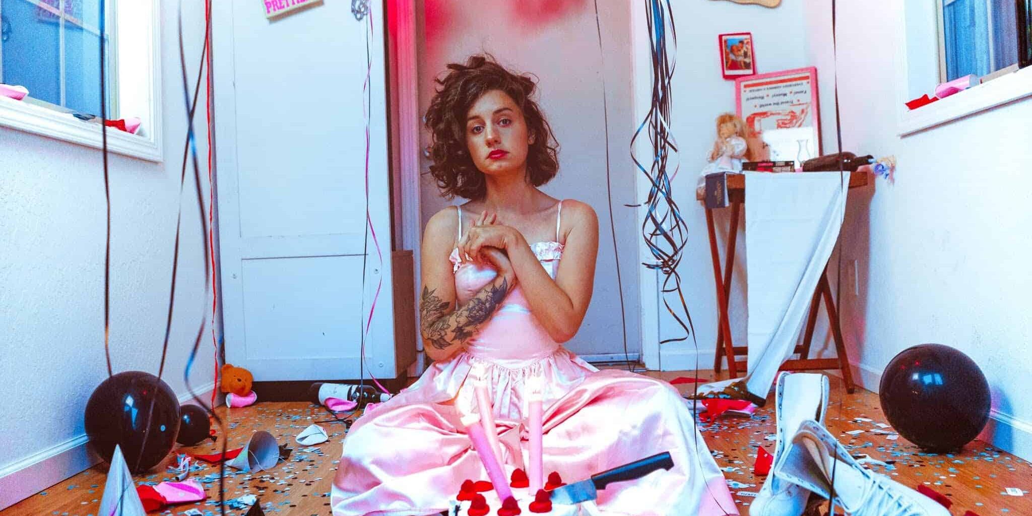Young woman in pink dress sitting with cake, balloons, and party decorations.
