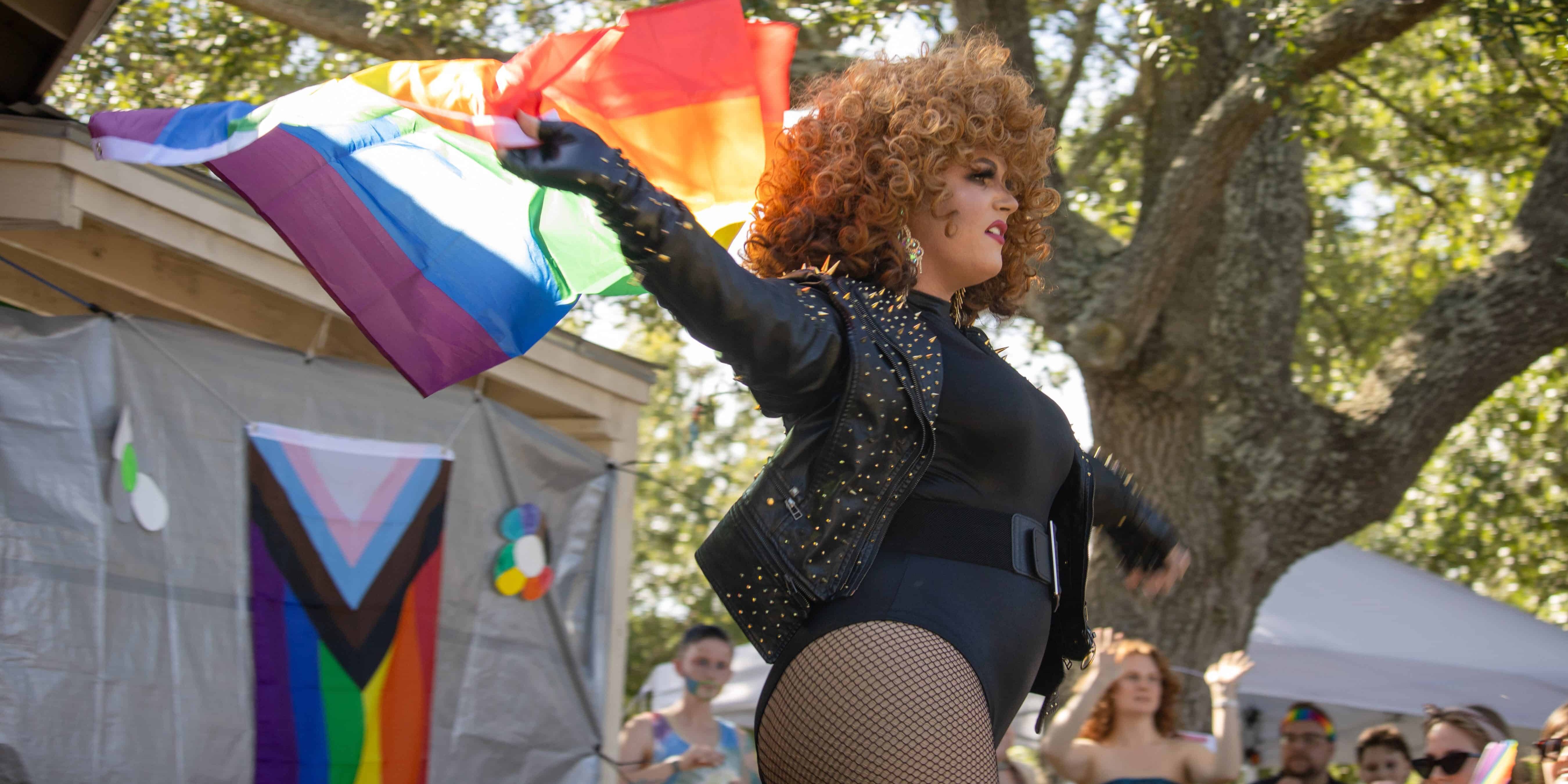 Woman waving rainbow pride flag at outdoor LGBTQ+ event.
