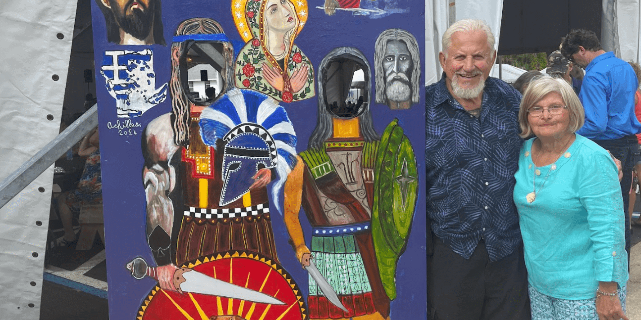 Colorful Greek festival display with cultural symbols and two smiling attendees.