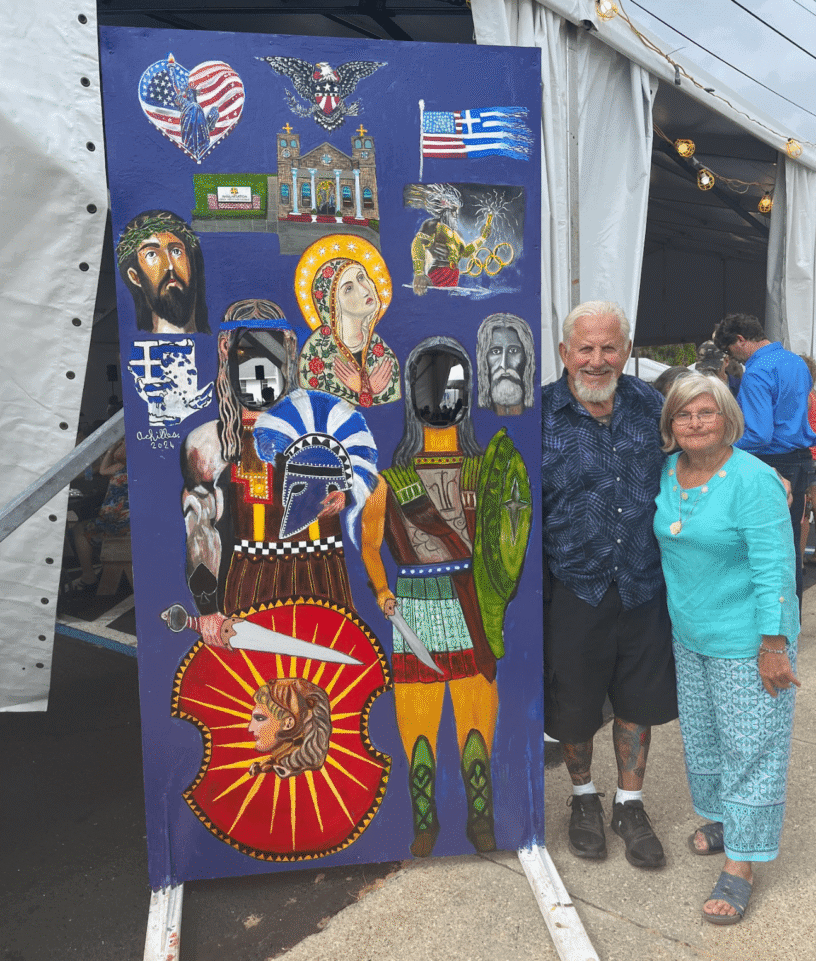 Colorful Greek festival display with cultural symbols and two smiling attendees.