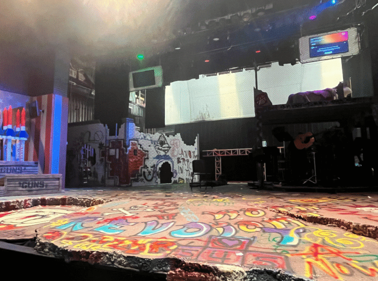 Stage setup with graffiti art and musical instruments for "The Son of Rage and Love" performance.