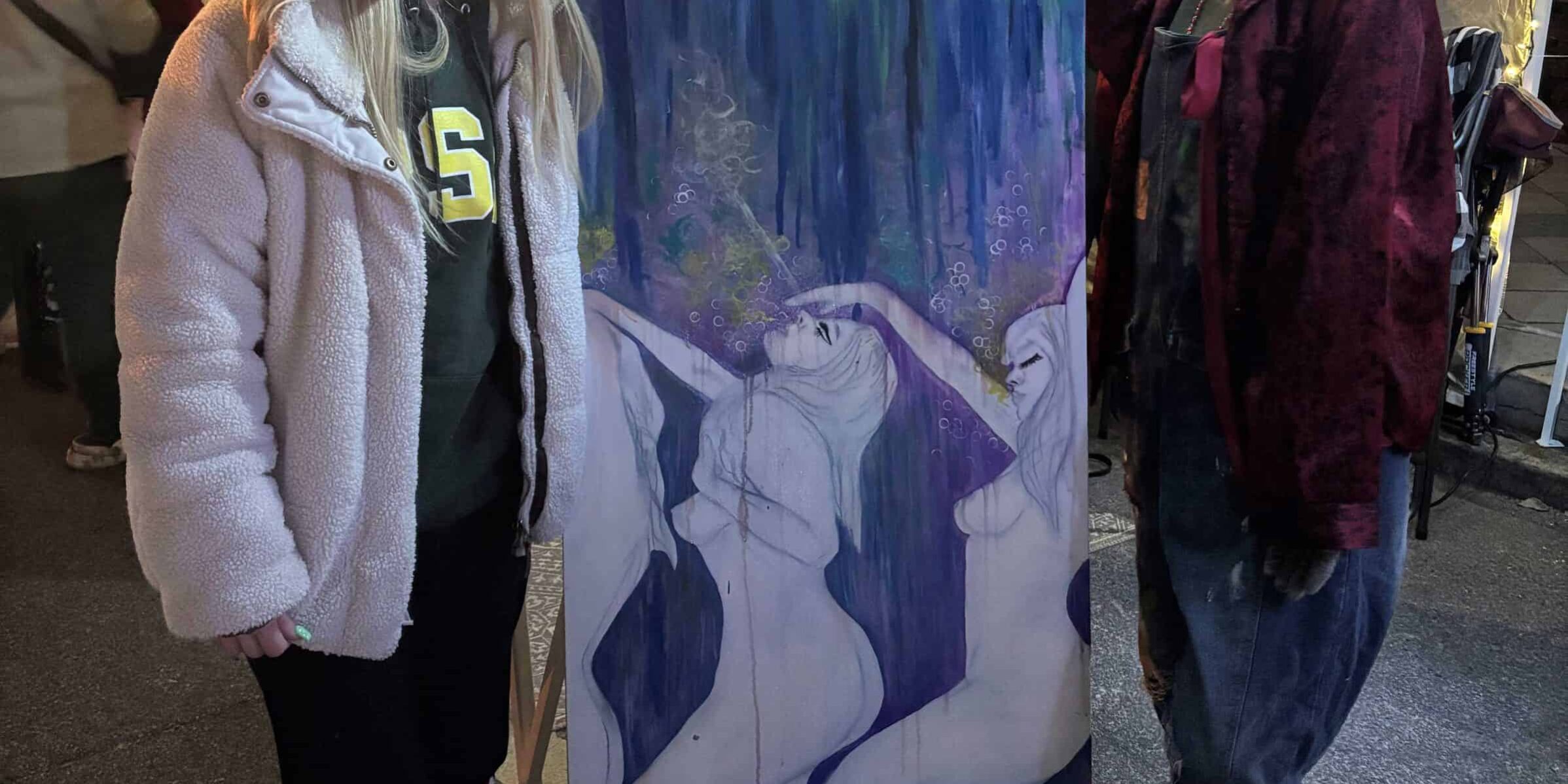 Two young women showcasing a colorful abstract painting at Pensacola's Gallery Night event.