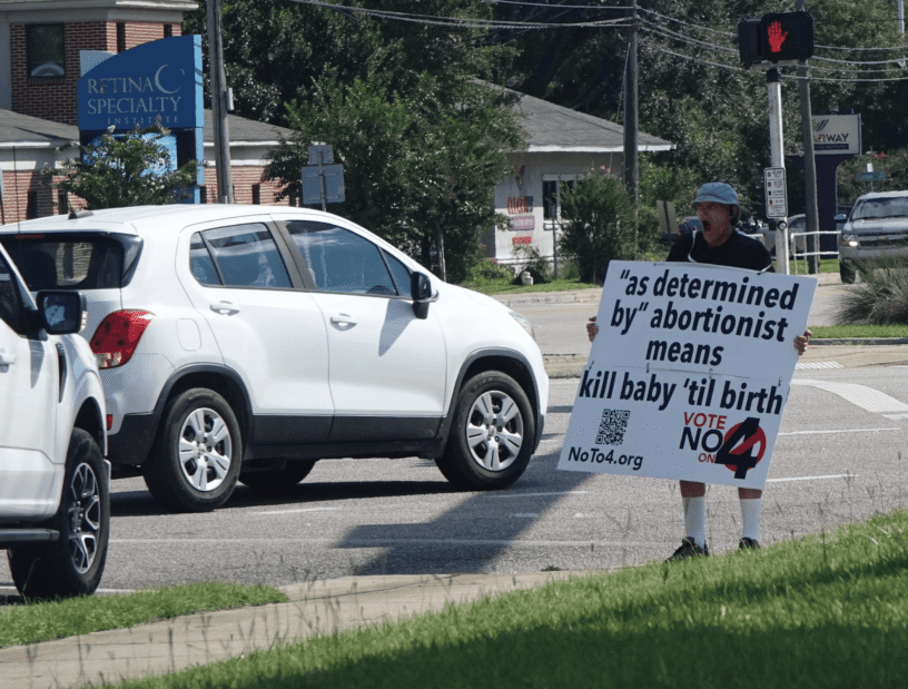 Person holding anti-abortion sign near traffic in Florida.