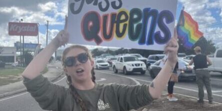 Woman protesting with a sign reading "No Kings yass Queens" at a rally.