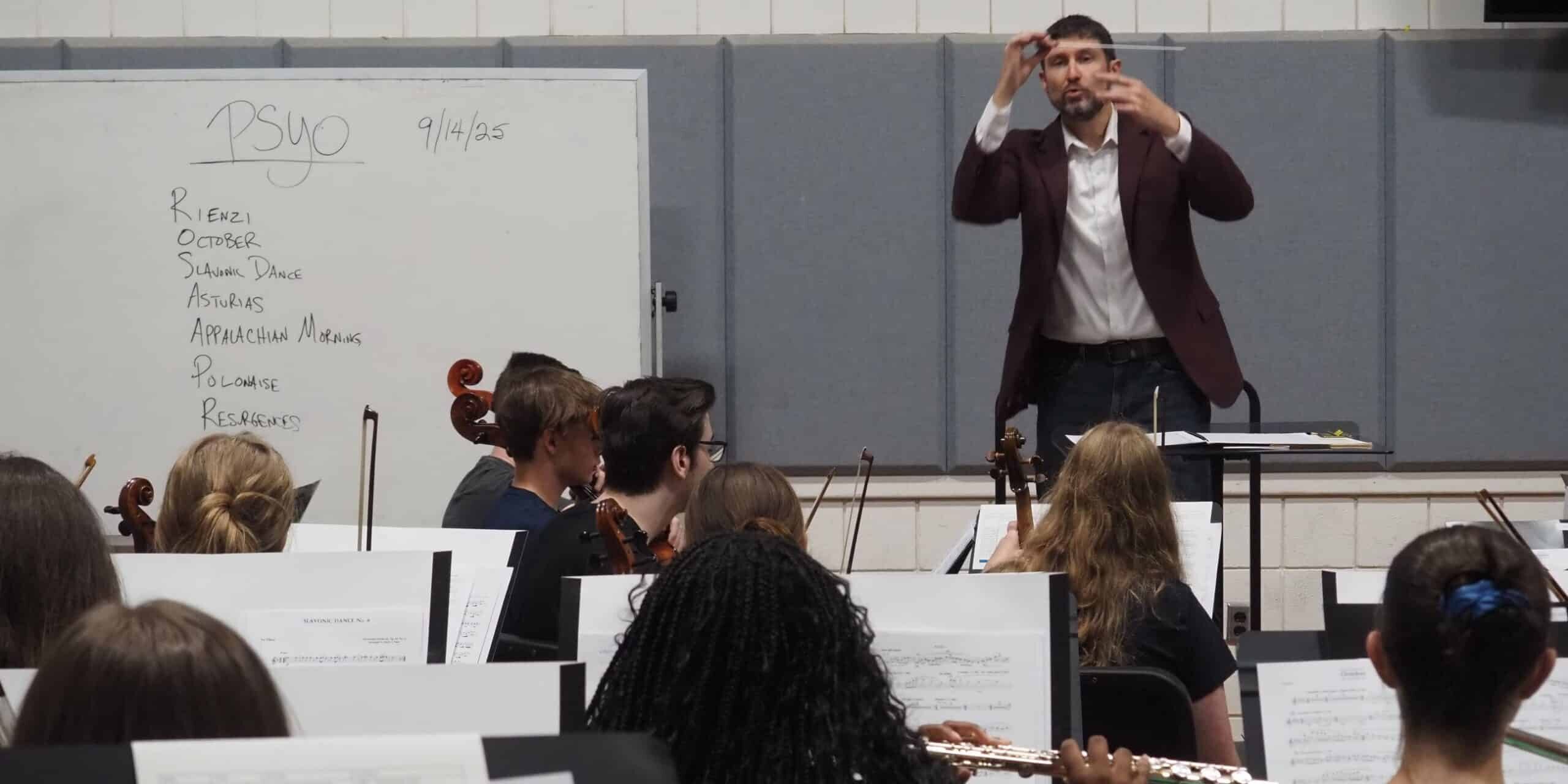 Music students practicing with conductor during youth orchestra rehearsal.