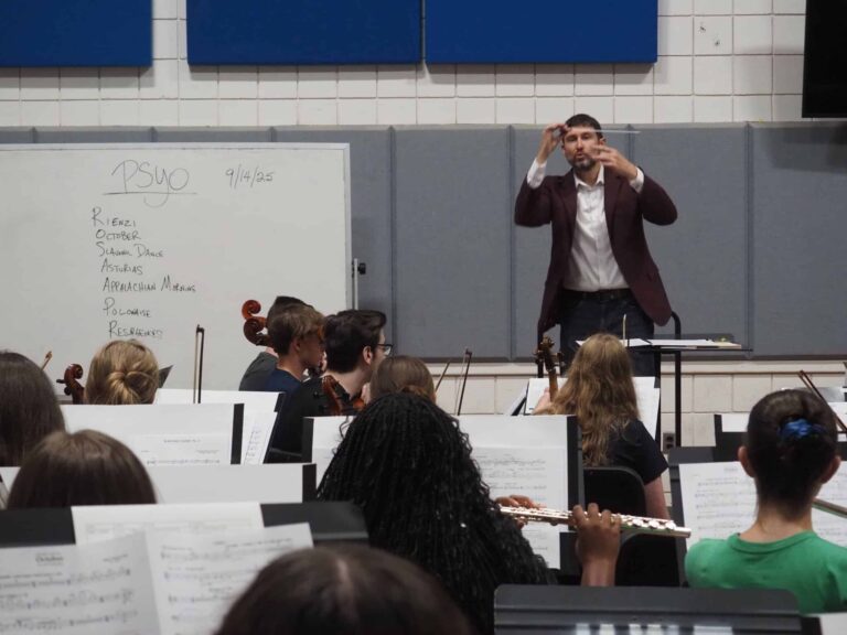 Music students practicing with conductor during youth orchestra rehearsal.