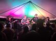 Live band performing at Pensacola’s Night Moves Festival under colorful tent lighting.